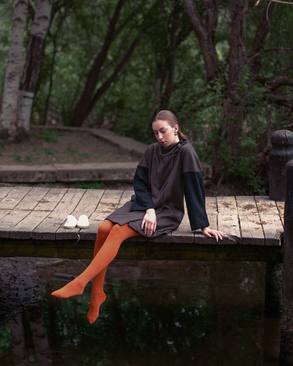 Mujer sentada en un puente usando un vestido oscuro sostenible de inspiración minimalista.