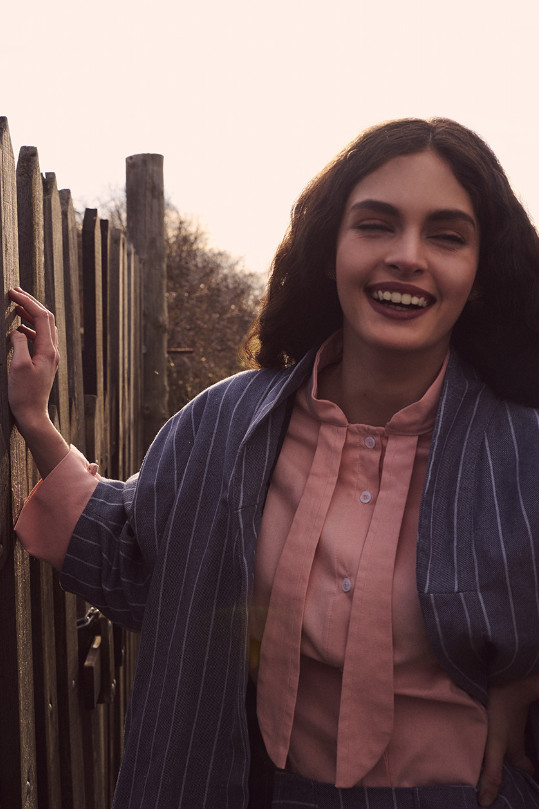 Mujer sonriendo con camisa rosa y chaqueta de rayas sostenibles, reflejando estilo consciente y alegría.